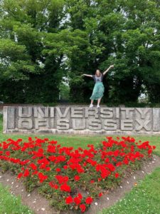 Anna standing on a large University of Sussex sign with her arms raised